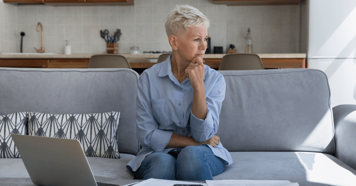 Senior woman sitting on couch with laptop on coffee table reviewing retirement income